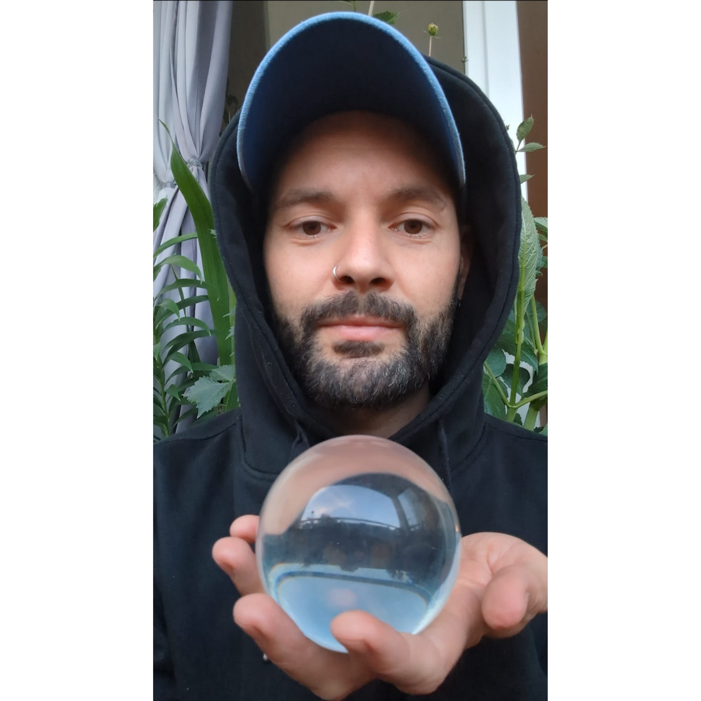 Man holding a clear glass ball in front of a window with plants